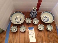 Top-down view of the porcelain set showing the two bowls, six sake cups, and vase with ruler in the background for scale.