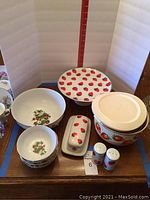 Full view of strawberry-themed serving set on a wooden table showing pie stand, butter dish, bowls, and shakers.