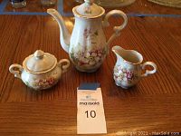 Set of three ceramic tea set pieces including teapot, sugar bowl, and creamer all hand painted with floral designs.