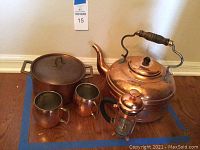 Wide shot showing entire copper set including kettle, pot, mugs, and mini French press on wooden floor