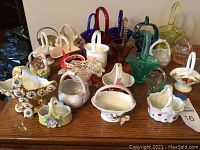 Photo showing assortment of small vintage baskets in glass, porcelain, bone china and brass in multiple colors and decorative styles arranged on wooden surface.