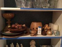 Shelf displaying wooden pedestal dish, trays, small wood decorative items, clock, clay vase, and candles.