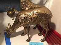 Close-up of two brass reindeer figures with detailed fur texture on a white surface marked with blue tape labeled 15 inches.