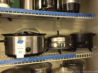 Shelf with three kitchen appliances: Cooks 6 quart slow cooker, Farberware electric skillet, Presto multi cooker kettle