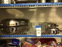 Stainless steel roaster, stainless steel pans with lids, and two glass mixing bowls on a wire shelf.