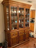Full view of large oak china cabinet with glass doors and wooden base with drawers and cabinets.