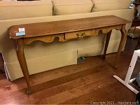 Full view of the Thomasville sofa table positioned against a couch, showing the wood color, drawer, and leg details.