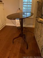 Side view of the oval tilt top table showing the pedestal base and three legs.