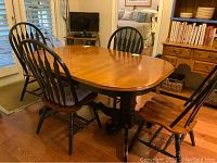 Dining table set in room, showing oval wood table top and six black chairs.