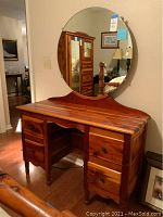 Front view of vintage cedar dressing table with attached round mirror reflecting room interior.