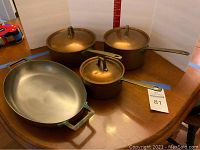 Four copper cookware pieces on wooden table against white board: oval baker, three lidded saucepans