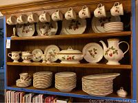 Wooden hutch with three shelves displaying cups hung on pegs, plates at back, stacks of saucers and dinnerware pieces.