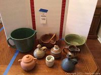 Full group shot of eight pottery items including pitchers, bowls, jars, and a mortar and pestle.
