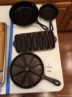 Four cast iron pans shown on a white surface including two cornbread pans with cob molds and two skillets