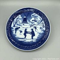 Front of the round blue and white porcelain collector plate depicting ice skaters and a windmill in a winter scene.