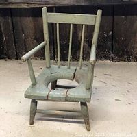 Front view of a vintage wooden child's potty chair painted green with a large crack in the seat and worn paint.