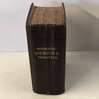 Front view of book spine showing gold embossed title Domestic Medical Practice on black textured cover with marbled page edges