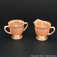 Side-by-side of the Fire-King cream pitcher and sugar bowl in peach lustre showing front and handles