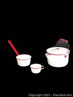 Full set of three vintage white enamelware pieces with red trim on black background: small cup, dipper, and pot with lid and handle.