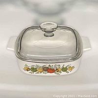 White ceramic rectangular CorningWare casserole dish with Spice of Life vegetable and herb decorative pattern on the side, glass lid with knob on top.
