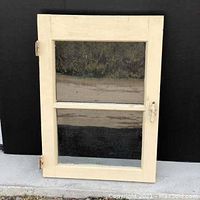 Front view of cream-colored vintage window with two glass panels reflecting surroundings.