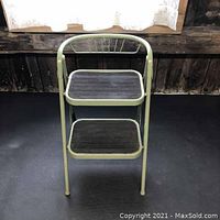 Front view of the vintage foldable step stool showing two black steps and curved green metal back frame.