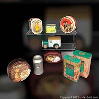 Full assortment of colorful vintage style collector tins displayed on a black background including truck, cocoa, biscuit, and fruit designs
