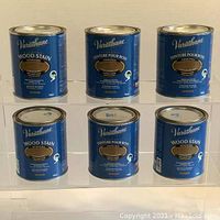 Front view of six blue cans of Varathane Wood Stain showing the label and product name, Golden Oak color.