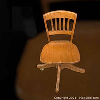 Front view of vintage oak desk chair showing seat, backrest slats, and caster wheels.