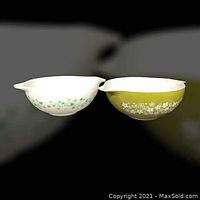 Two vintage Pyrex 4-quart Cinderella mixing bowls side by side: one with white and green Spring Blossom Crazy Daisy floral pattern, the other olive green with white Ivy floral motif. Both have pouring spouts and handles.