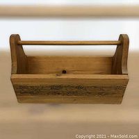 Front view of wooden wine caddy showing carved grapevine design on front panel and central handle.