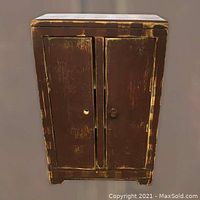 Front view of small wooden child's toy cupboard with two doors, showing wear and one missing knob.