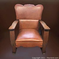 Front view showing leather upholstered seat and backrest, broad wooden armrests, and carved wooden legs of the Mission style rocking chair.