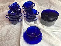 16 cobalt blue glass teacups and 15 matching saucers stacked and arranged on cloth
