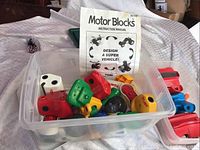 Plastic bin containing assorted Tomy Motor Blocks parts in multiple colors with visible instruction manual.