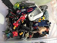 Top view of large bin filled with various action figures and toy vehicles showing diverse shapes and colors