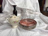 Front and side view of amethyst vase, sugar bowl with floral pattern and lid, clear glass ribbed bud vase, clear glass pitcher, pink depression divided dish with chrome holder