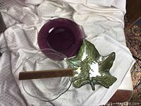 Clear glass wave-inspired salad bowl, purple glass charger, and one iridescent green glass leaf-shaped serving dish on light fabric background