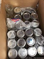 Top-down view of multiple clear glass Ball mason jars packed in a cardboard box, showing several jars with lids and bands.