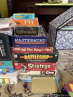 Stacked board game boxes with various classic titles visible including Rook, Pit, Rummikub, Mastermind, All The King's Men, Battleship, and Stratego.