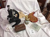 Photo showing overall lot contents including microscope, wooden disc washer box, glass slides, leather water bag, Washington DC mug, and magic rings.