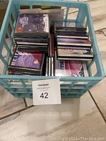 Top-down view of a blue plastic crate filled with stacked classical and easy listening CDs, showing varied titles and artworks.