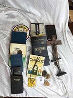 Overview of the lot showing AA and religious books, crucifixes, medal, rosary, cross stones, and other items arranged on white fabric.