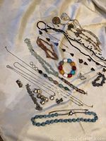 Overview of assorted necklaces, bracelets, and button covers spread on fabric showing variety and colors.