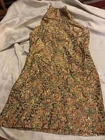 Gold thread cocktail dress with jewel-toned floral pattern laid out flat