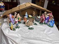Full view of ceramic nativity set arranged with wooden stable in the background on a cloth-covered surface