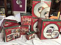 Photo shows boxed sets of 'A Christmas Story' dinnerware by International China including dinner plates, mugs, tumblers, teacups, saucers, and serving bowls.