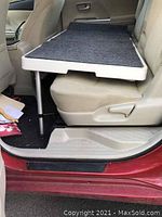 Shelf installed over rear car seats showing black non-sliding carpet surface and telescoping legs resting on floor and seat.