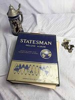 Photo showing Statesman Deluxe Album binder, vintage German stein, and old keys laid out on white fabric