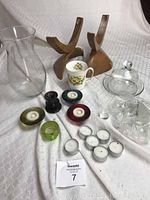 Photo showing oak candelabras, bone china teacup, clear vase, assorted tea light holders, and small glass shot glasses or tea light holders with various candles.